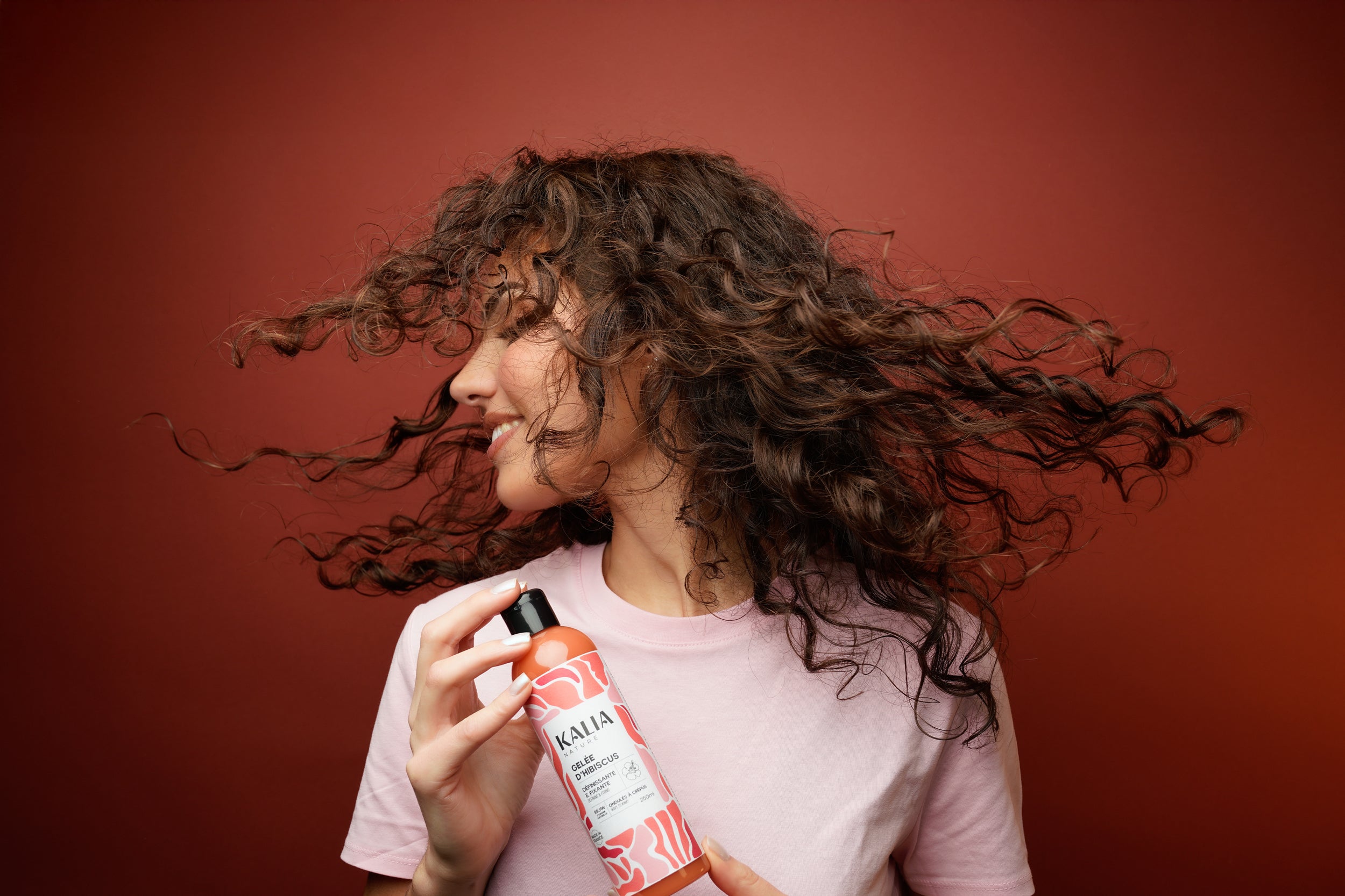 Portrait d’une femme avec la gelée d’hibiscus de Kalia Nature dans les mains, faisant virevolter ses cheveux.