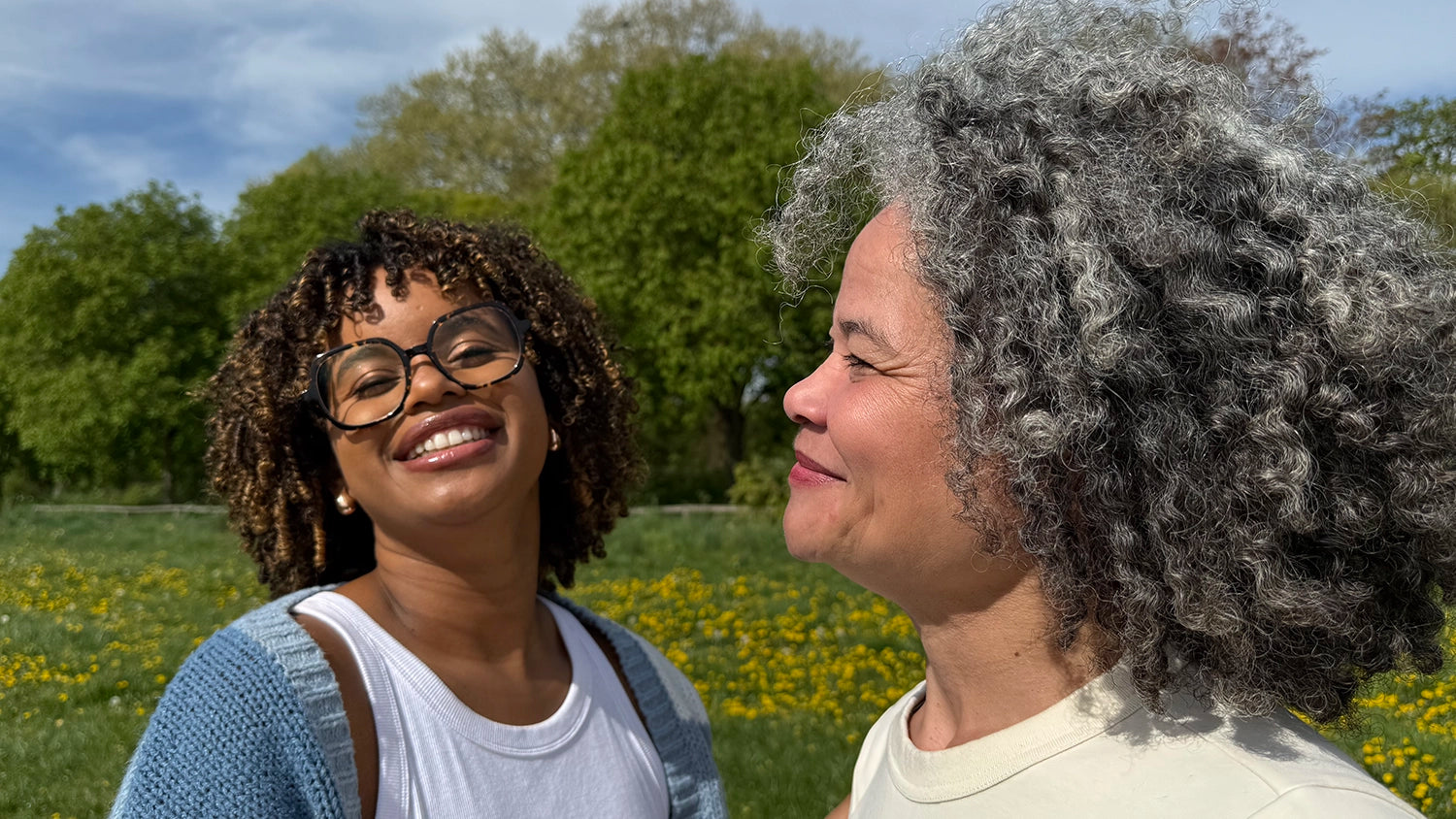 Photo de deux femmes complices aux cheveux frisés, en extérieur, pour Kalia Nature.